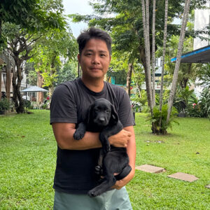 Khách hàng bế chó Labrador con màu đen chụp ngoài trời trên bãi cỏ, nền cây xanh