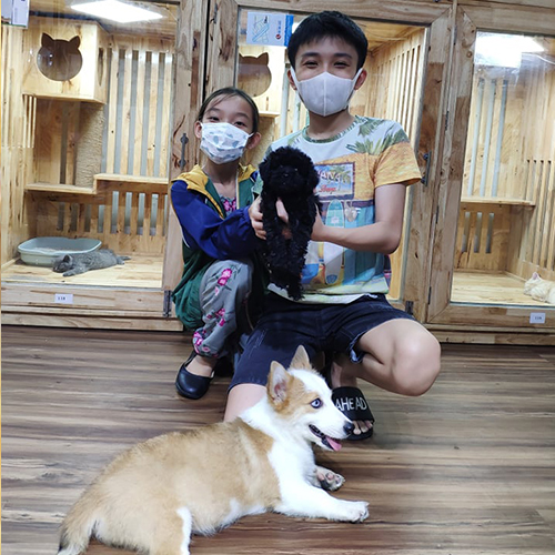 Hai bạn nhỏ lựa chó Poodle đen tại Chạm Pets Family, bé Poodle được bồng trên tay trong khu vực chọn bé