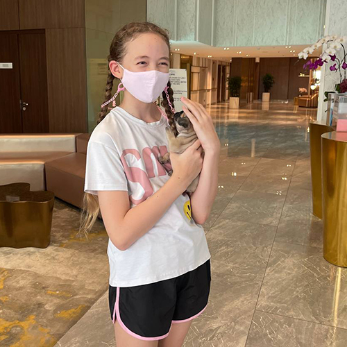 Bé gái đeo khẩu trang ôm chó Pug con trong sảnh, khoảnh khắc thân thiện và bám chủ