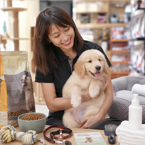 Cô gái bế chó Golden con bên cạnh thức ăn, dây dắt, lược chải và đồ chăm sóc thú cưng